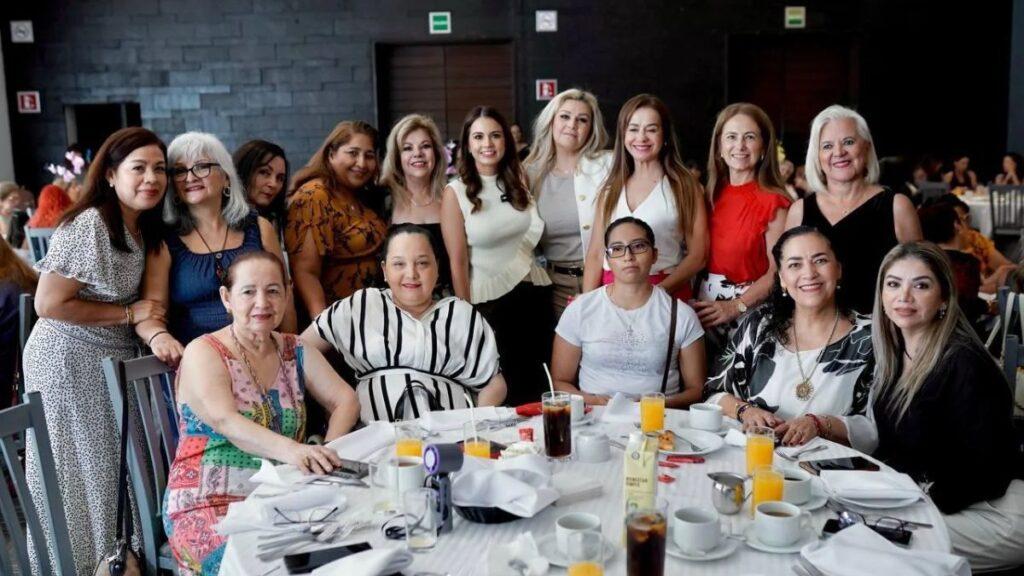 Lorena-de-la-Garza-fortalece-apoyo - CRONICAS REGIAS Group of women posing around a round table at a catered event, with drinks and plates in front of them on a banquet hall setting.