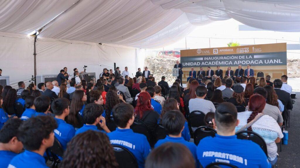Inauguration ceremony at a university, with officials on stage inside a white tent and a seated audience in blue shirts facing them.
