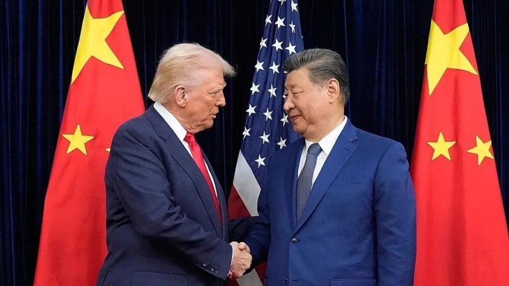 Two men in dark suits shake hands in front of alternating US and Chinese flags behind them.