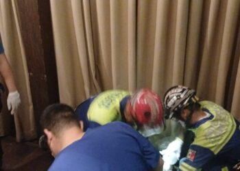 Emergency responders in blue and yellow uniforms kneeling around a person on the floor near beige curtains.01/2024: image shows responders providing aid indoors. (informative)