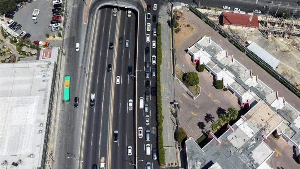 Aerial view of a multilane highway with cars and a curved overpass, bordered by a green bus and surrounding buildings