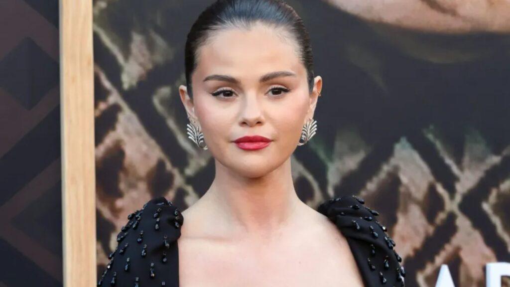 Close-up portrait of a woman with slicked-back hair, red lipstick, and ornate leaf-shaped earrings wearing a black beaded dress at a formal event.